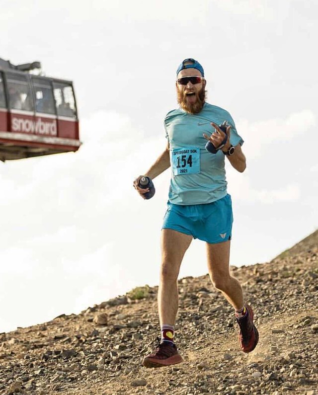 Zach running down a rocky mountain trail in a race bib, tongue out, with a tram car overhead